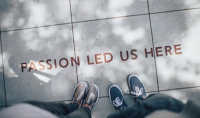 two pairs of feet in shoes on sidewalk with passion led us here written on sidewalk