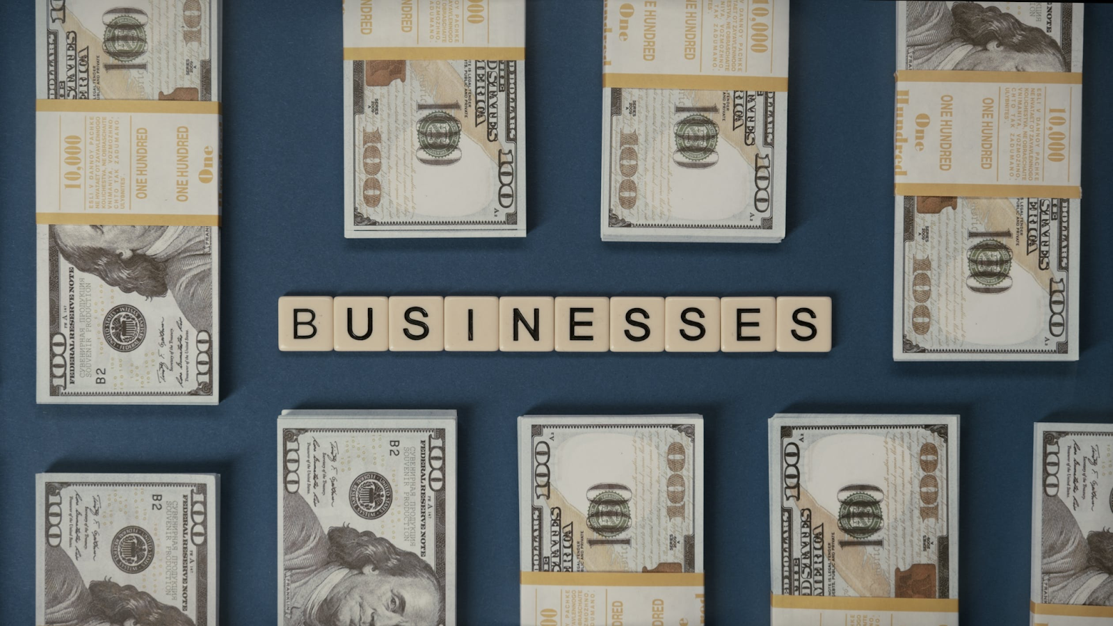 nine stacks of 100 hundred dollar bills scramble tiles spell businesses how businesses operate